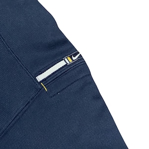 Puede incluir: Primer plano de tela azul marino con un parche rectangular. El parche presenta una franja blanca con un dise&ntilde;o amarillo y negro, y un peque&ntilde;o logotipo de Nike. Se ve una costura amarilla.