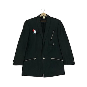 May include: Black blazer with silver zippers on the pockets and front. The blazer has a pocket square with red and white accents. The blazer is hanging on a wooden hanger.