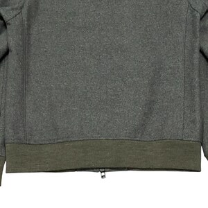 May include: A gray wool jacket with a dark olive green ribbed hem and cuffs. The jacket has a zipper closure. The fabric has a textured appearance.