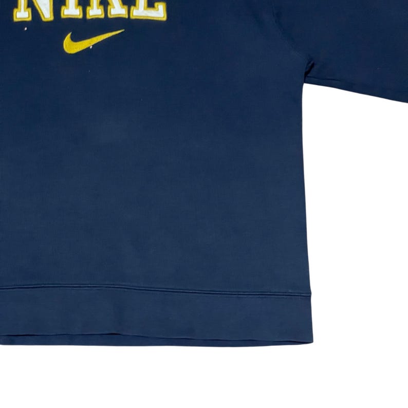 Puede incluir: Sudadera azul marino con la palabra "NIKE" en letras amarillas y un logotipo de Nike en forma de swoosh amarillo. La sudadera tiene cuello redondo y mangas largas. La tela parece ser un material suave y c&oacute;modo.