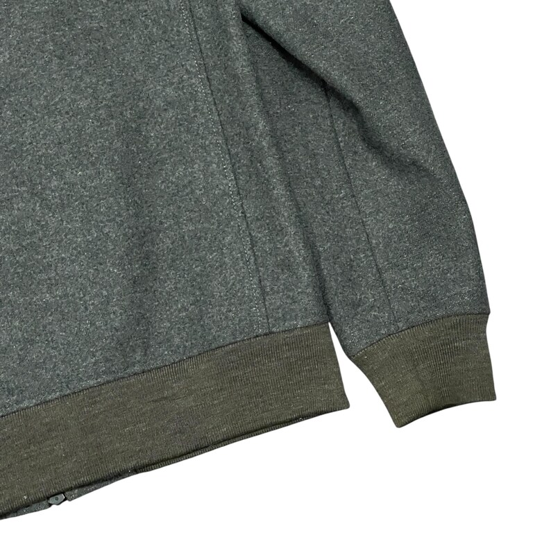May include: A close-up of a gray jacket with a dark green ribbed hem and cuffs. The jacket has a zipper and a seam detail running down the sleeve. The fabric appears to be a wool blend.