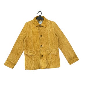 May include: Mustard-colored jacket with a textured finish, featuring a collared neckline, button-down closure, and two front pockets. The jacket is hanging on a black hanger. A small tag is visible near the collar.