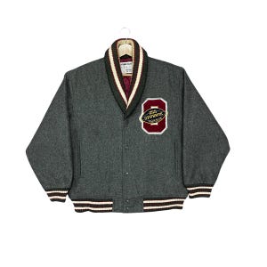 May include: A charcoal gray wool-blend varsity jacket featuring a shawl collar with dark green and white stripes. The jacket has a maroon quilted lining and a patch on the left chest that reads OFFENSE 1967 CLUB with a football graphic.