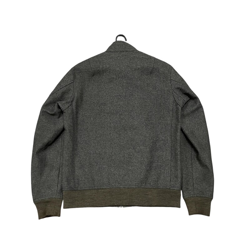 May include: A charcoal gray bomber jacket with a ribbed olive green hem and cuffs. The jacket is hanging on a black hanger against a white background. The back of the jacket is visible.