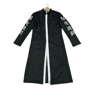 May include: Black long coat with white trim and Japanese text on the sleeves. The coat has a stand-up collar and a full-length design. The coat is hanging on a hanger against a white background.