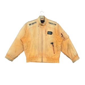 May include: An orange vintage jacket with the text "NEW CONCEPTER" and "POWERED-RJ2W" printed on it. The jacket has a zip-up front, multiple pockets, and a stand-up collar. The jacket is made of a durable material.