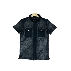 May include: Black short-sleeved jacket with a snakeskin pattern. The jacket features a zip-up front, two chest pockets with button closures, and a contrasting black collar and shoulder panels. The jacket is hanging on a wooden hanger.