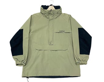 May include: A light green anorak-style jacket with black sleeves and a high collar. The jacket has a front pocket and the brand name "mont-bell" is printed on the chest. The jacket is hanging on a white hanger.