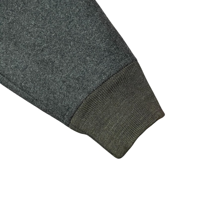May include: Close-up of a gray sweatshirt sleeve with a ribbed, olive green cuff. The fabric has a textured appearance, and the sleeve is angled, showing the seam where the cuff is attached.