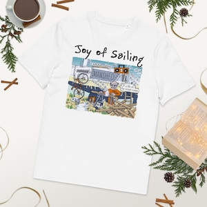 以下が含まれることがあります： カラフルな漫画のグラフィックが施された白いTシャツ。グラフィックには「Joy of Sailing」の文字と、「EMANSHED」と「WAAA」の文字が入ったボートのシーンのイラストが描かれています。