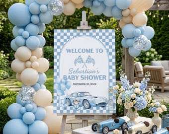 以下が含まれることがあります： 「Sebastian's Baby Shower」と書かれた看板があるベビーシャワーのシーン。看板にはヴィンテージカーのイラストが描かれ、青とクリーム色の風船に囲まれています。おもちゃのレーシングカーとフラワーアレンジメントが、お祝いの装飾を完成させています。