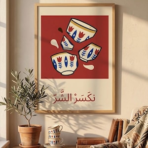 Op de afbeelding: Een ingelijste kunstprint met een rode achtergrond, met gestileerde gebroken theekopjes. De theekopjes hebben een witte basis met blauwe en rode bloemmotieven. De print bevat Arabische tekst.
