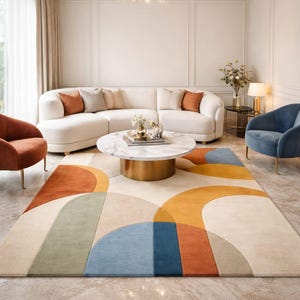 May include: A modern living room featuring a cream-colored curved sofa with orange and neutral pillows. A round marble coffee table sits on a colorful geometric rug with orange, blue, and beige shapes. Two accent chairs and a chandelier complete the space.