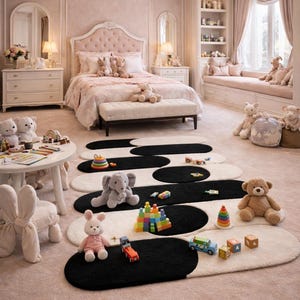 K&ouml;nnte beinhalten: Ein rosa Schlafzimmer mit einem gro&szlig;en Bett, einer Bank und passenden M&ouml;beln. Auf dem Boden liegen ovale schwarz-wei&szlig;e Teppiche, auf denen Spielzeug und Stofftiere verstreut sind. Eine Leuchte h&auml;ngt von der Decke.