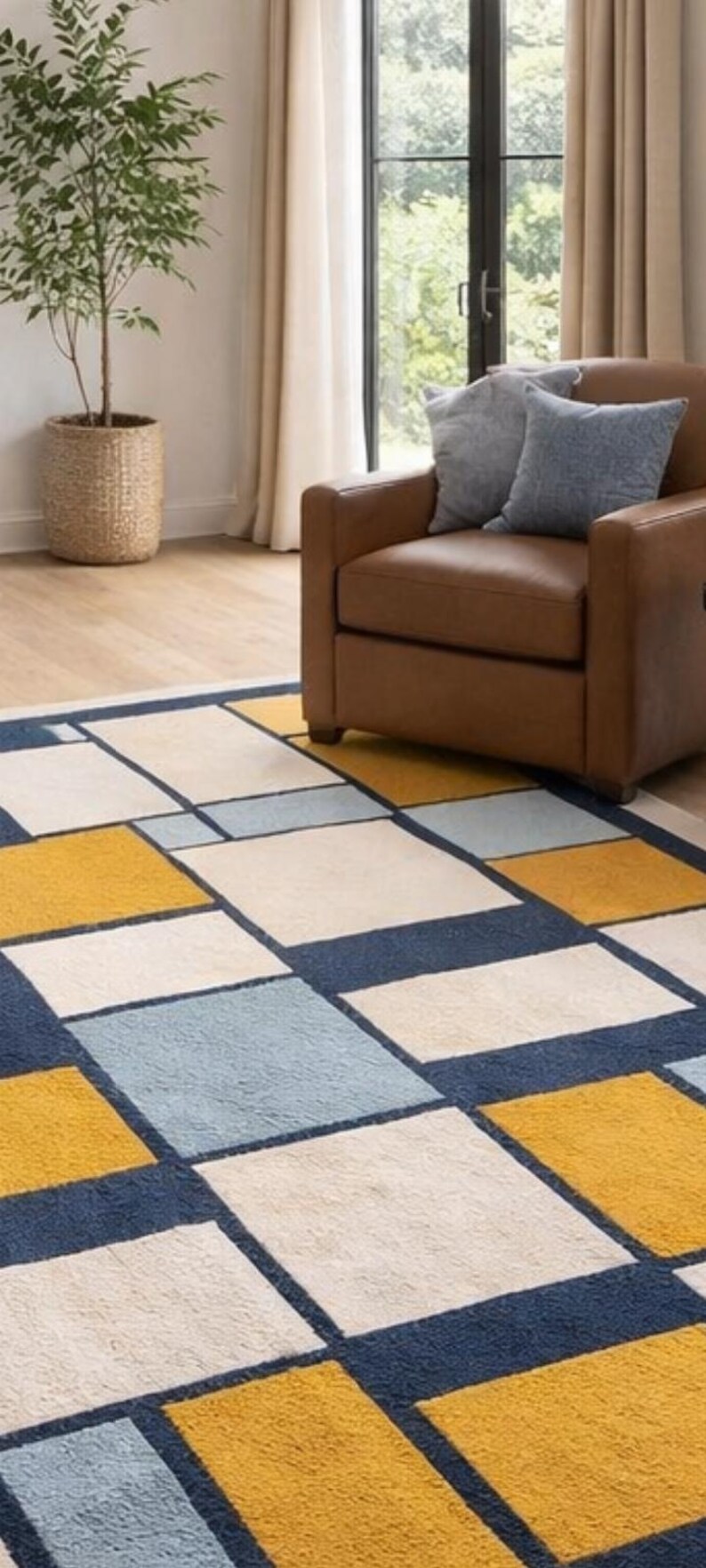 May include: Geometric patterned area rug with a modern design. The rug features a grid of squares in navy blue, mustard yellow, light blue, and cream colors. The rug is placed in a living room setting with a brown leather armchair.