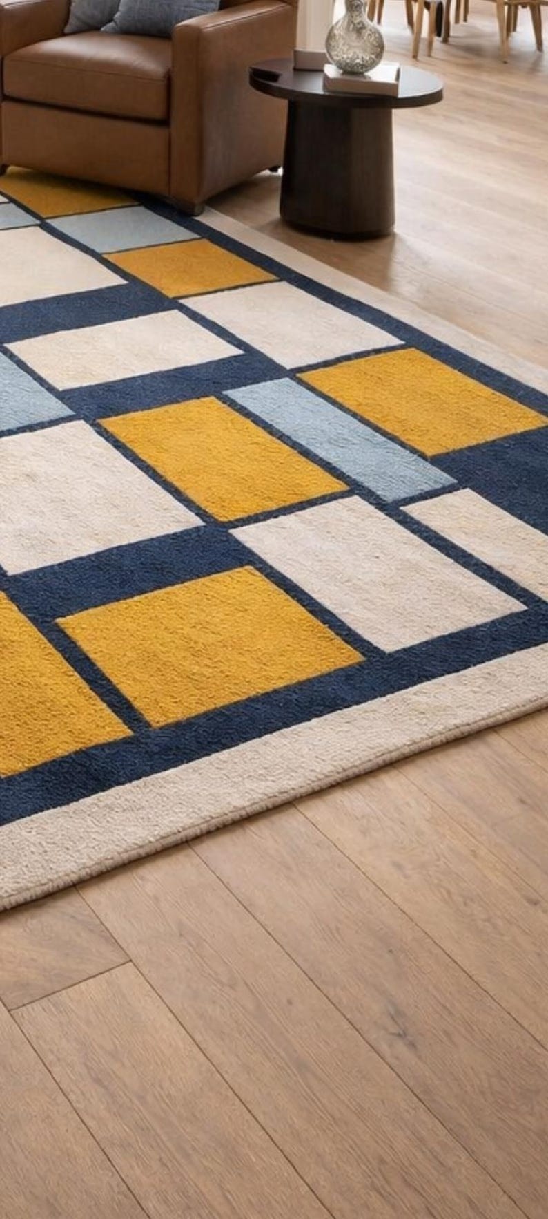 May include: A rectangular area rug with a geometric pattern. The rug features squares in cream, navy blue, light blue, and mustard yellow. The rug is placed on a hardwood floor.