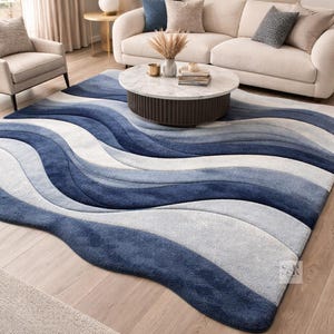 May include: A large, rectangular area rug with a wave-like design in shades of blue and gray. The rug is placed in a living room setting, with a sofa, armchair, and coffee table visible in the background.