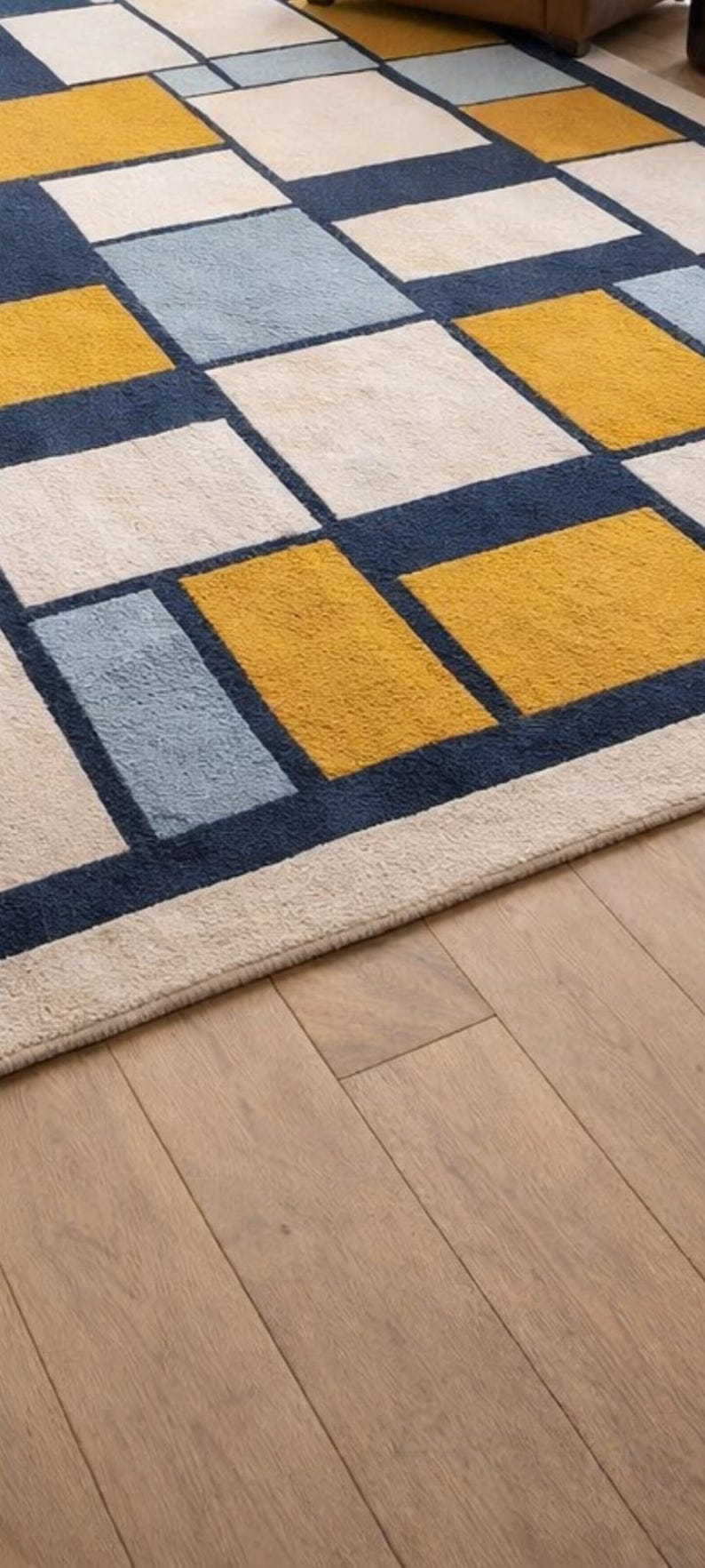 May include: Geometric patterned rug featuring a grid of rectangles in navy blue, cream, light blue, and mustard yellow. The rug is placed on a hardwood floor.