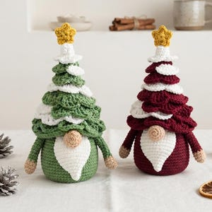 May include: Two crochet gnome figurines shaped like Christmas trees. One gnome is green with white accents, and the other is deep red with white accents. Both feature a yellow star on top, a round beige nose, and a white beard on a round base.