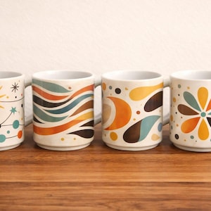 May include: Four ceramic mugs with retro designs. Each mug has a different pattern: a starburst, wavy lines, abstract shapes, and a flower. The mugs are white with colourful accents and sit on a wooden surface.