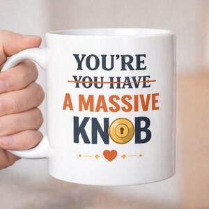以下が含まれることがあります： 白のセラミックマグカップ。紺色とオレンジ色で「YOU'RE A MASSIVE KNOB」と書かれています。「YOU HAVE」の文字は取り消し線で消されています。金色のドアノブのグラフィックと赤いハートも特徴です。