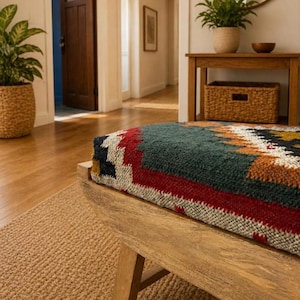 Peut inclure: Un banc en bois doté d'une assise en textile épais tissé avec un motif géométrique dans des tons bleu sarcelle, rouge, orange, blanc et noir. Le banc possède une structure en bois clair naturel avec des pieds robustes sur un tapis beige.