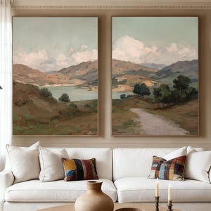 May include: Two framed landscape paintings hang above a white sofa with colourful throw cushions. A round wooden coffee table holds a vase, bowl, and books. A bronze sculpture and floor lamp are on the left.