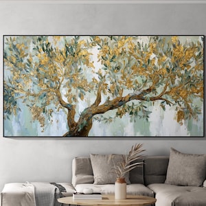 May include: An olive tree painting with gold and green leaves and a brown trunk. The artwork is in a black frame and hangs above a gray sofa. The painting has a textured, abstract style.