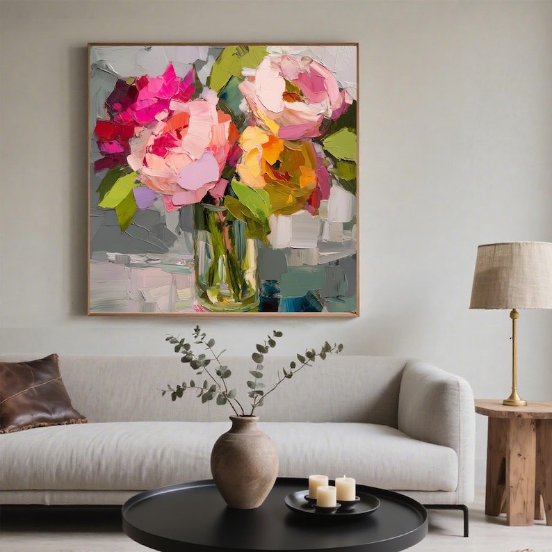 May include: An abstract painting of a floral arrangement in a clear glass vase. The flowers are a mix of pink, orange, and yellow, with green leaves. The painting is in a wooden frame and hangs on a light gray wall.