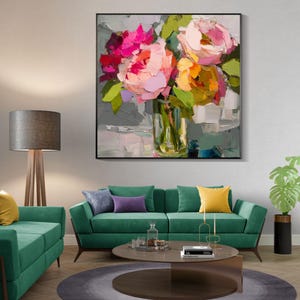 May include: A framed floral oil painting featuring a bouquet of pink, red, and yellow flowers in a clear glass vase. The artwork has a textured, impressionistic style with visible brushstrokes. The painting is displayed above a green sofa.