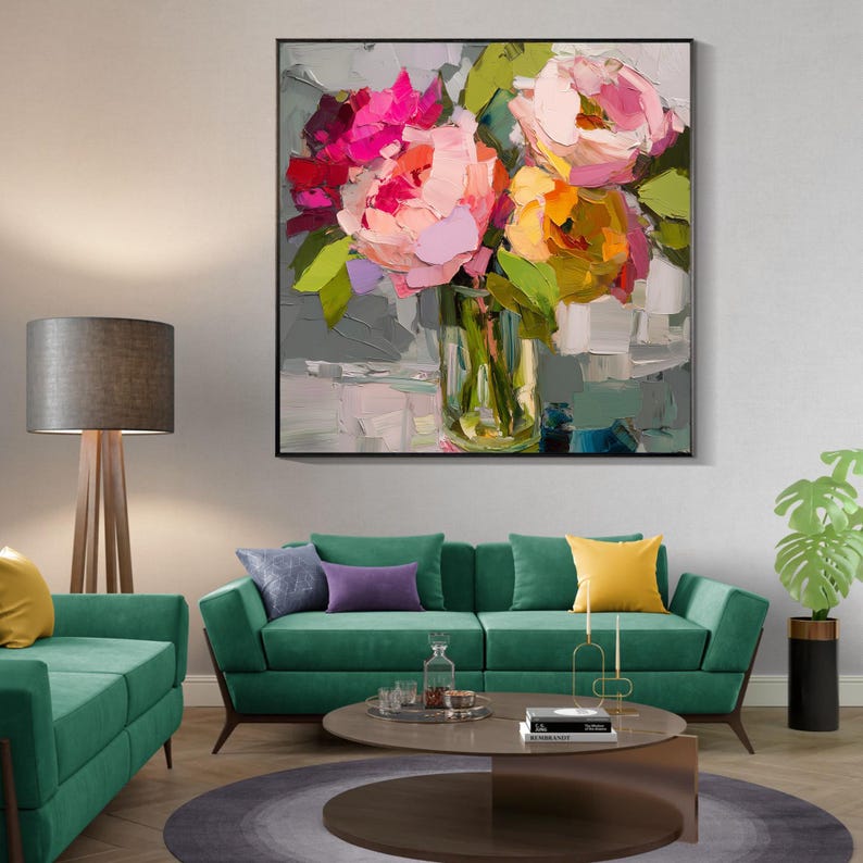 May include: A framed floral oil painting featuring a bouquet of pink, red, and yellow flowers in a clear glass vase. The artwork has a textured, impressionistic style with visible brushstrokes. The painting is displayed above a green sofa.