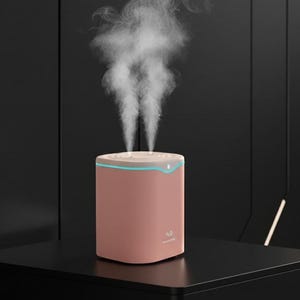 Op de afbeelding: Een roze en witte luchtbevochtiger met een blauw licht en twee stoomstralen. De luchtbevochtiger is vierkant met afgeronde hoeken en de tekst "H2O" op de voorkant. Hij staat op een zwart oppervlak.