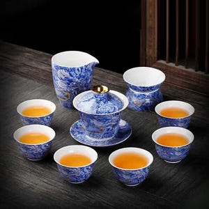 Op de afbeelding: Een blauw-wit porseleinen theeservies met een drakenmotief. De set bevat een theepot met deksel, een melkkan, een serveerstandaard en zes theekopjes gevuld met thee. De theeset wordt gepresenteerd op een donkere houten ondergrond.