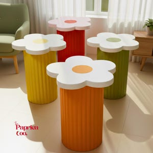 May include: Four colorful flower-shaped side tables. Each table has a white flower-shaped top with a colored center. The cylindrical bases are yellow, red, green, and orange. The tables are in a bright, modern interior setting.