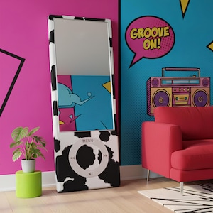 May include: A full-length mirror with a black and white cow print design. The mirror is shaped like a music player with a circular control panel at the bottom. The background features a pink and blue wall with pop art elements.