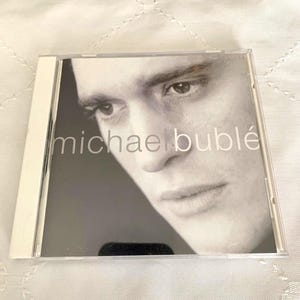 May include: A standard clear plastic CD jewel case featuring the self-titled Michael Bublé album cover. The artwork displays a black and white close-up portrait of a person's face with the text michael bublé printed in a clean, lowercase font.