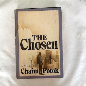 May include: A hardcover book titled The Chosen, a novel by Chaim Potok. The cover features a muted illustration of a person standing near a building entrance with steps. The title is printed in large black serif font against a cream background.
