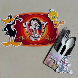 Peut inclure: Un ensemble de fête sur le thème des Looney Tunes avec une pancarte rectangulaire, des découpes de Daffy Duck, Titi et Vil Coyote. Inclut un porte-couverts noir avec Bugs Bunny contenant un couteau pailleté, une fourchette et une cuillère blanches.