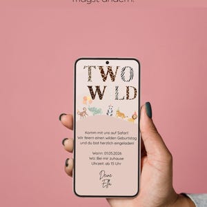 Könnte beinhalten: Ein Smartphone zeigt eine 'Two Wild' Geburtstagseinladung mit Safari-Tierillustrationen. Die Einladung enthält deutschen Text mit Datum, Uhrzeit und Ortsangaben. Das Telefon wird vor einem rosa Hintergrund gehalten.
