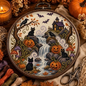 Puede incluir: Un bordado de punto de cruz circular en un bastidor de madera que muestra una escena de Halloween con una cascada, tres gatos negros, tres calabazas, una casa con techo morado, cuervos, murciélagos y setas coloridas sobre tela clara.