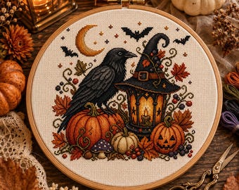 Può includere: Un telaio da ricamo circolare in legno contenente un disegno a punto croce di un corvo nero appollaiato su una zucca arancione accanto a una lanterna illuminata, un cappello da strega, foglie autunnali, bacche, una zucca intagliata e una luna.