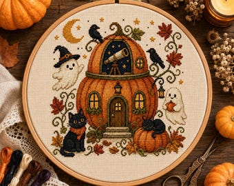 May include: A circular embroidery hoop containing a cross-stitch pattern of a pumpkin house. The design features a black cat, two ghosts, a telescope in an upper window, crows, and autumn leaves on a cream-colored fabric background.
