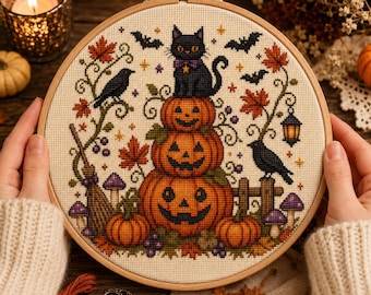 Può includere: Un telaio da ricamo circolare in legno contenente un motivo a punto croce di un gatto nero seduto sopra una pila di tre zucche di Halloween arancioni. Il disegno include pipistrelli neri, due corvi, foglie d'acero autunnali e una lanterna.