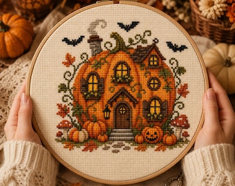 Può includere: Un telaio da ricamo circolare in legno contenente un motivo a punto croce di una casa a forma di zucca. Il design presenta una grande zucca arancione modellata come un cottage con finestre, una porta, un camino, viti verdi e pipistrelli.