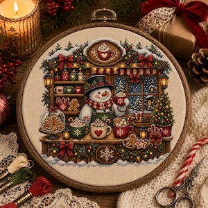 Peut inclure: Un tambour à broder circulaire présentant une broderie au point de croix d'un bonhomme de neige dans une boutique servant du chocolat chaud. Le motif inclut des tasses, des biscuits, un sapin de Noël et des décorations festives sur tissu beige.