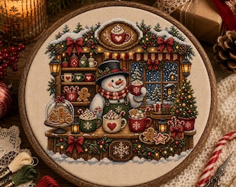 Può includere: Un telaio da ricamo circolare contenente un disegno a punto croce di un pupazzo di neve in un negozio che serve cioccolata calda. La scena presenta tazze, biscotti di pan di zenzero, un albero di Natale e decorazioni festive su tessuto beige.