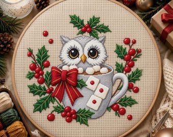 Può includere: Un ricamo a punto croce in un telaio di legno raffigurante un gufo grigio seduto in una tazza azzurra piena di marshmallow. Il disegno è decorato con foglie di agrifoglio verdi, bacche rosse e un grande fiocco rosso con bordo oro.