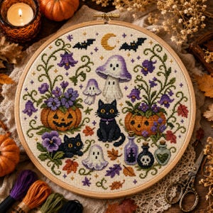 May include: A circular cross-stitch embroidery in a wooden hoop featuring two orange jack-o'-lanterns, two black cats, three ghosts, a purple mushroom, and various purple flowers, green vines, and autumn leaves on a cream-coloured fabric background.