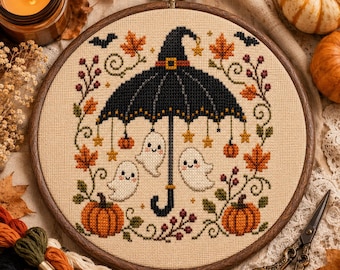 Può includere: Un telaio da ricamo circolare in legno contenente un motivo a punto croce su tessuto beige. Il design presenta un ombrello a forma di cappello da strega nero con tre fantasmi bianchi, zucche arancioni, foglie autunnali e piccole stelle.
