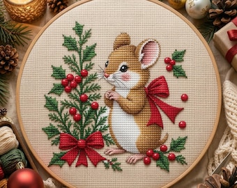 Può includere: Un ricamo a punto croce in un telaio circolare in legno raffigurante un topo marrone con la pancia bianca, in piedi accanto a un agrifoglio verde decorato con bacche rosse e un grande fiocco rosso. Il disegno è su tessuto beige.